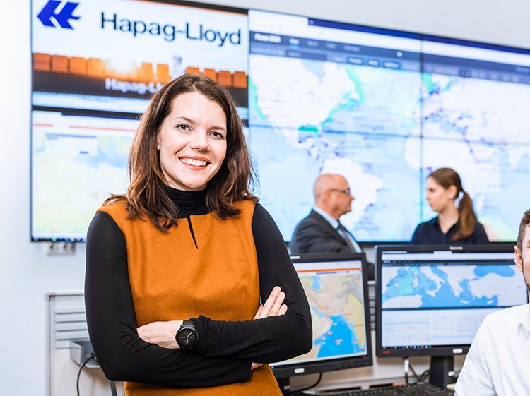 Eine Frau vor Bildschirmen und einem Hapag-Lloyd-Logo im Hintergrund.