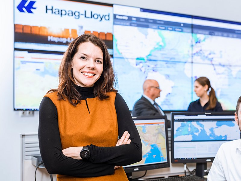 Eine Frau vor Bildschirmen und einem Hapag-Lloyd-Logo im Hintergrund.